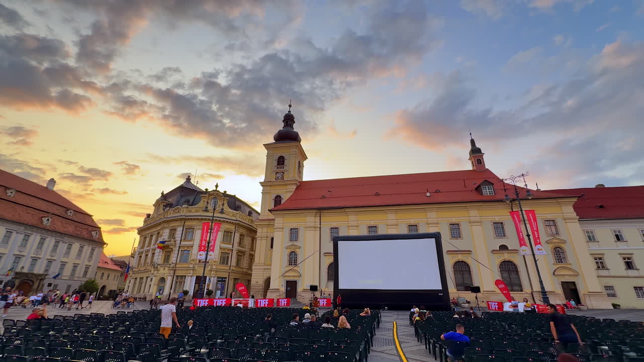 Sibiu, Romania, 17 July 2025: Large screen and multiple chairs for audience at square of Sibiu, Romania. Low angle view at the historical buildings of the city at sunset time