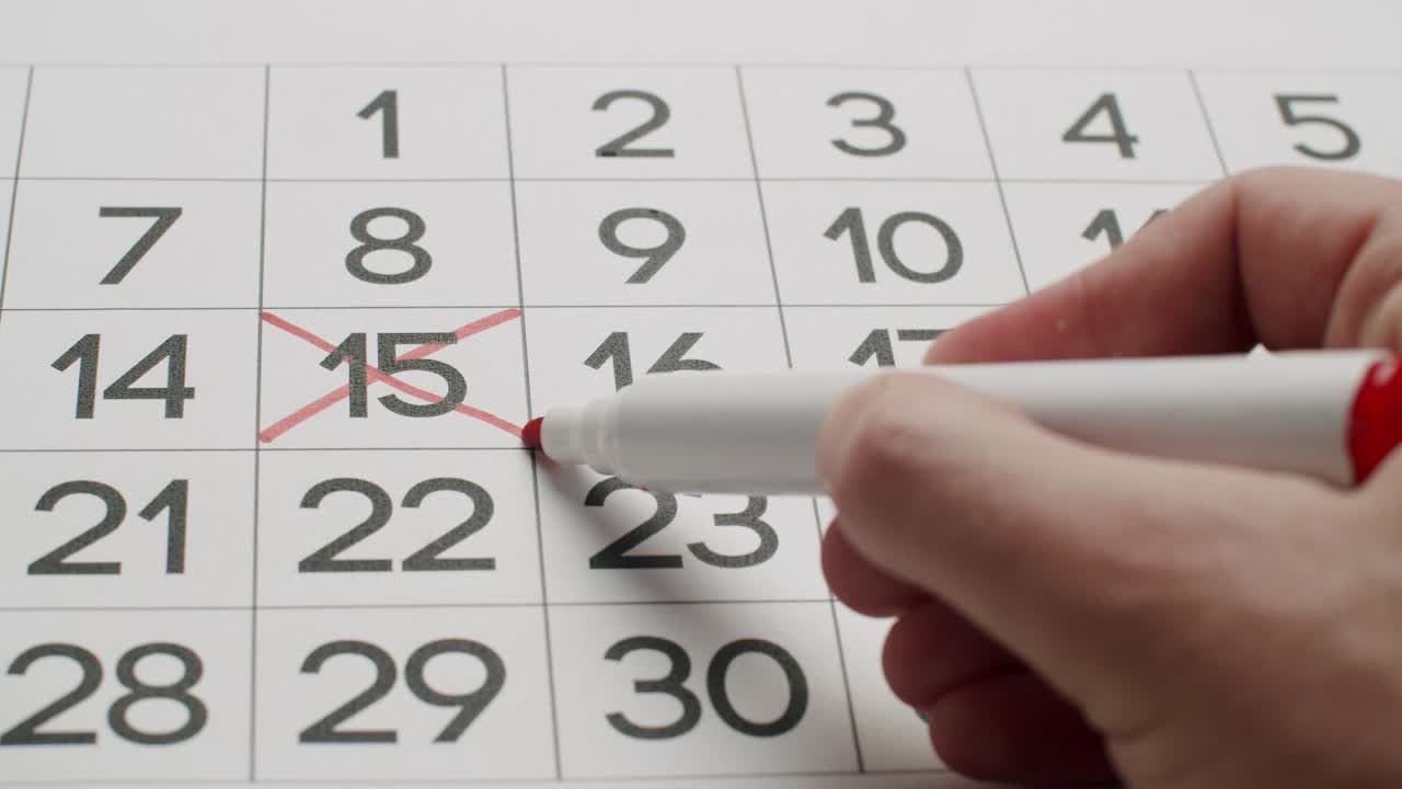 la mano del hombre escriba el día 23 en el calendario de papel usando un bolígrafo rojo.