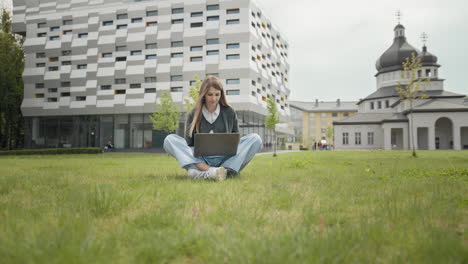 busy attractive girl working at the laptop as sitting on grass in city park on hectic summer morning