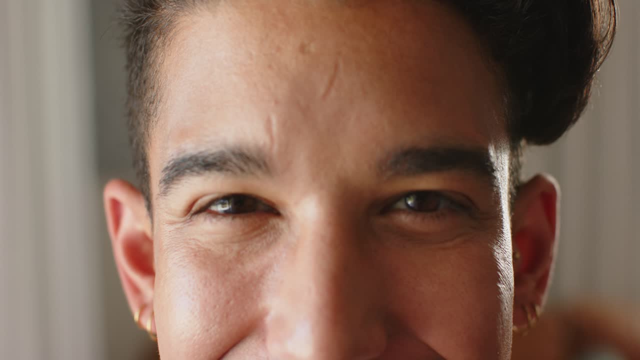 Male late twenties reacting to soft warm window light, blinking, smiling with gold hoops