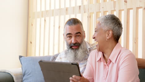 senior couple sitting on couch, using tablet and smiling together