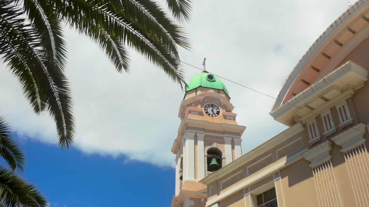 la torre del reloj de un edificio histórico en gibraltar - la catedral de santa maría la coronada, enmarcada por hojas de palma bajo un cielo parcialmente nublado