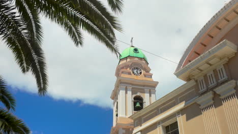 the clock tower of a historic building in gibraltar - cathedral of st mary the crowned, framed by palm tree leaves under a partly cloudy sky