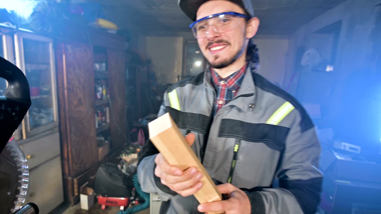 joven carpintero barbudo concentrado con gafas de protección y una gorra comprueba la pieza de trabajo