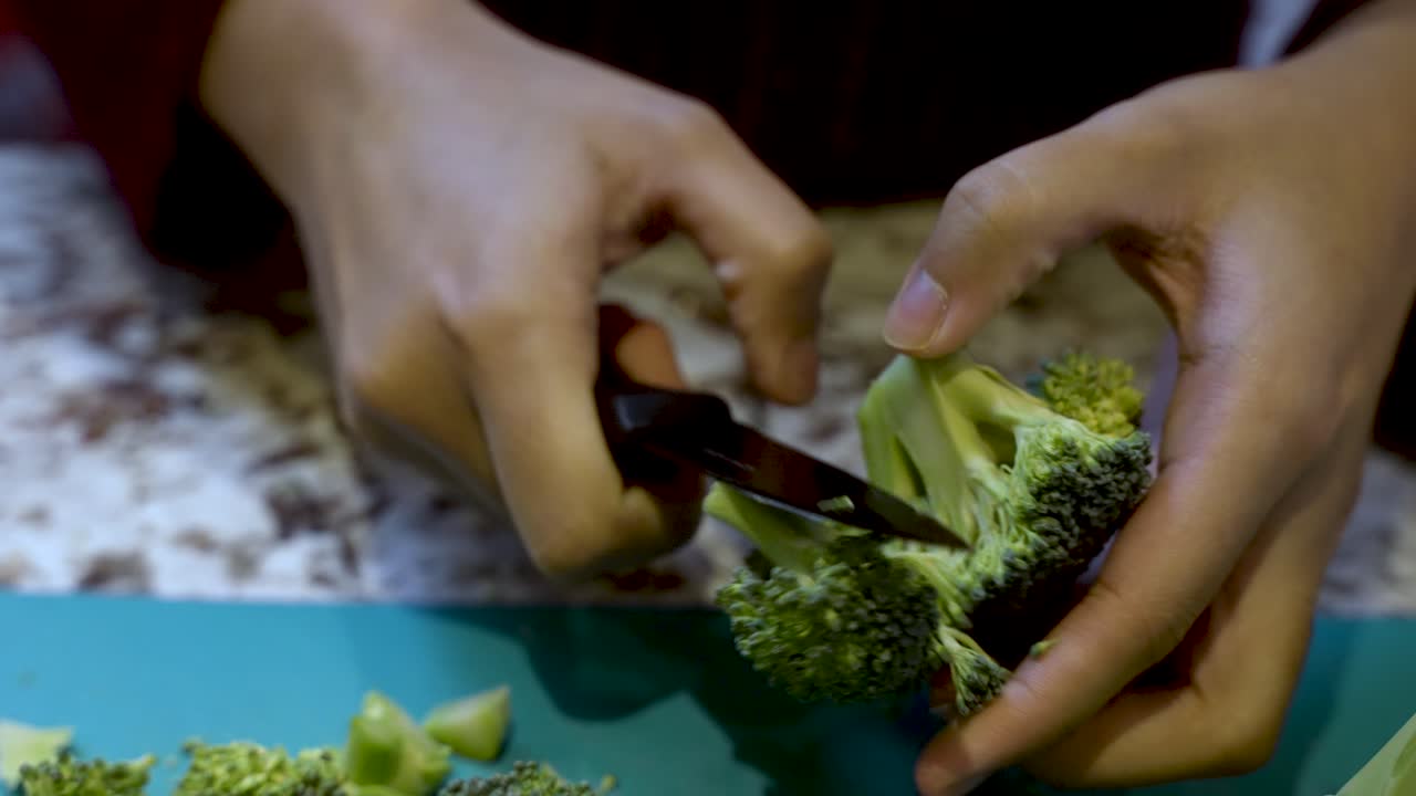 Hands Of Young Asian Woman Carefully Slicing Broccoli Over Cutting Board