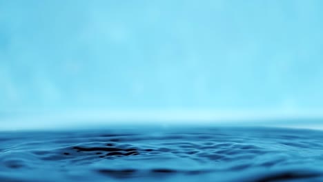 slow motion 4k video of a water surface with falling drops on a blue background. splashing water. studio shooting.