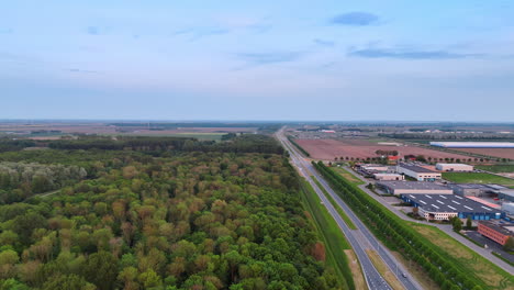 flight over the green forest and highways passing nearby. approaching storehouses in the countryside in the netherlands. aerial view.