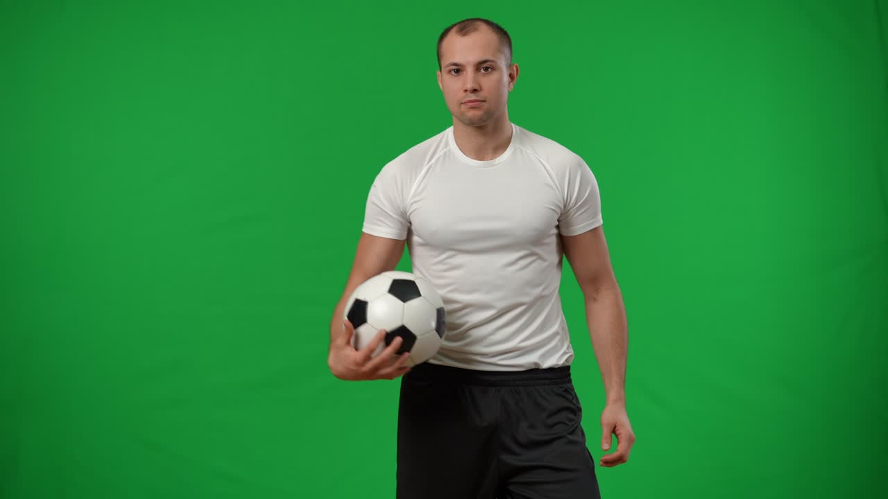 프로 카우카시안 축구 선수가 을 잡고 가으로 포즈를 취하고 있다.그린 스크린에 서 있는 카메라를 바라보는 자신감 넘치는 잘생긴 젊은 남자의 초상화.