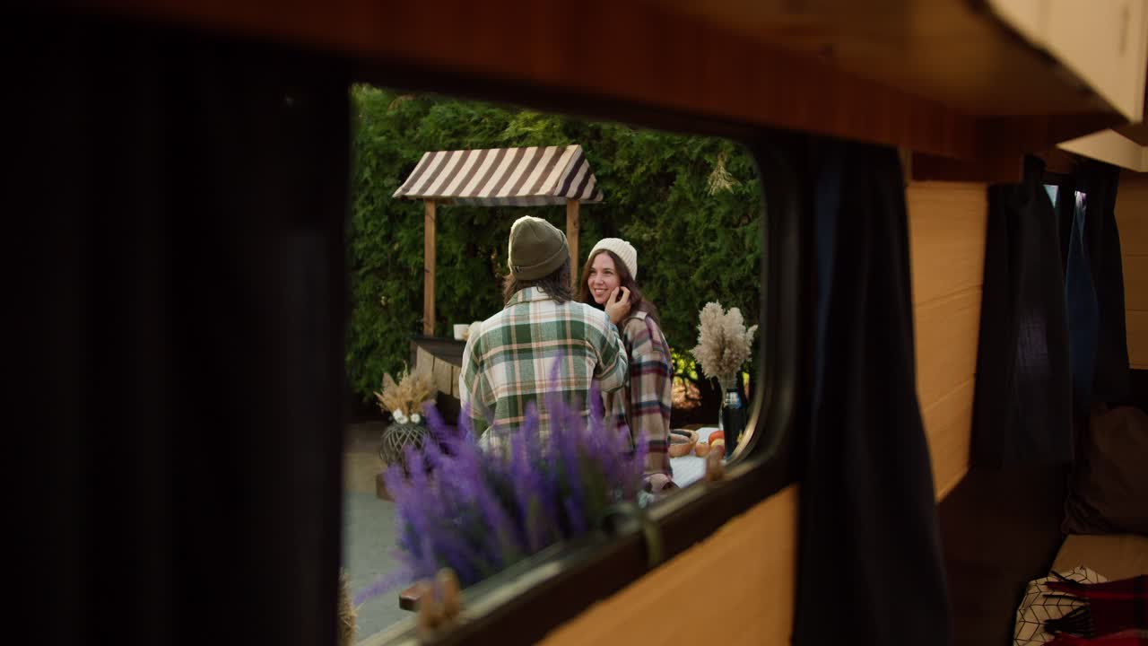Shooting in a trailer, a brunette man in a green checkered shirt strokes his brunette girlfriend on the cheek and communicates with her during his picnic at a camp outside the city in the summer
