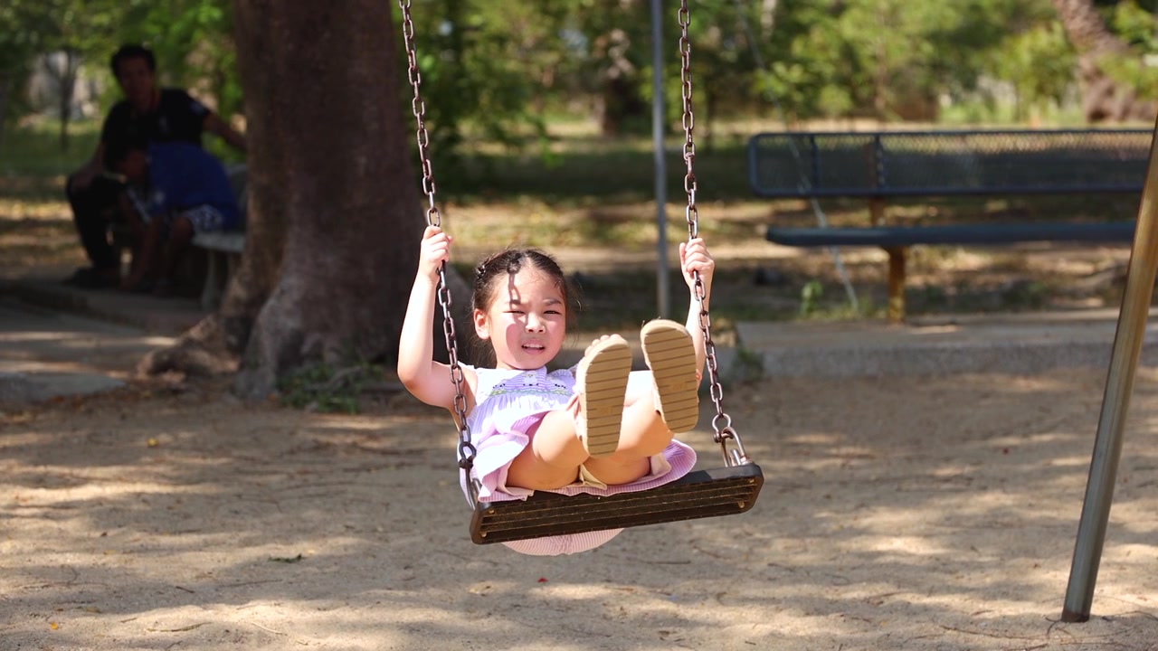 Una giovane ragazza asiatica con un vestito viola dondola felicemente su un'altalena nel Parco Lumpini.