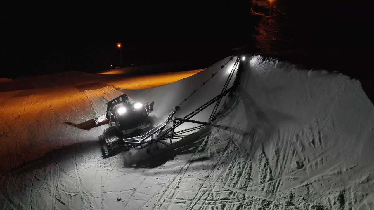 Aerial drone following snowcat grooming ski slope in winter mountains of Aomori Japan