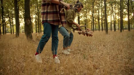 close-up shot of a man and a girl walking through a autumn forest and collecting firewood for a fire during a rest stop during a hike