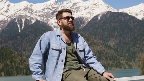 man sitting by a lake with snow-capped mountains