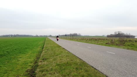 Drone-shot-of-motorcyclist-driving-by-between-grass-fields