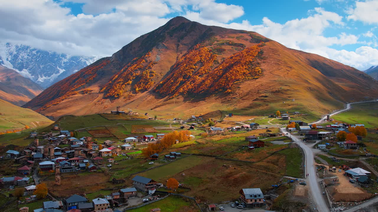 Kafkas Dağları'nda ortaçağ kulelerine sahip pitoresk eski köy üzerinde uçuş. Turuncu ormanlar kayaları kaplıyor. Ushguli, Yukarı Svaneti, Gürcistan