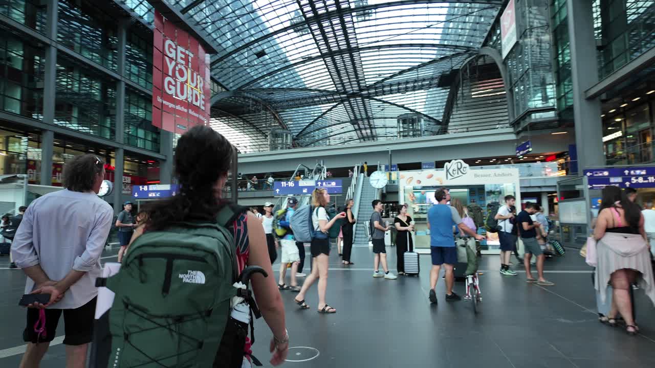 A bustling scene inside Berlin Central Station, capturing the dynamic atmosphere as people navigate the urban space with backpacks and luggage.