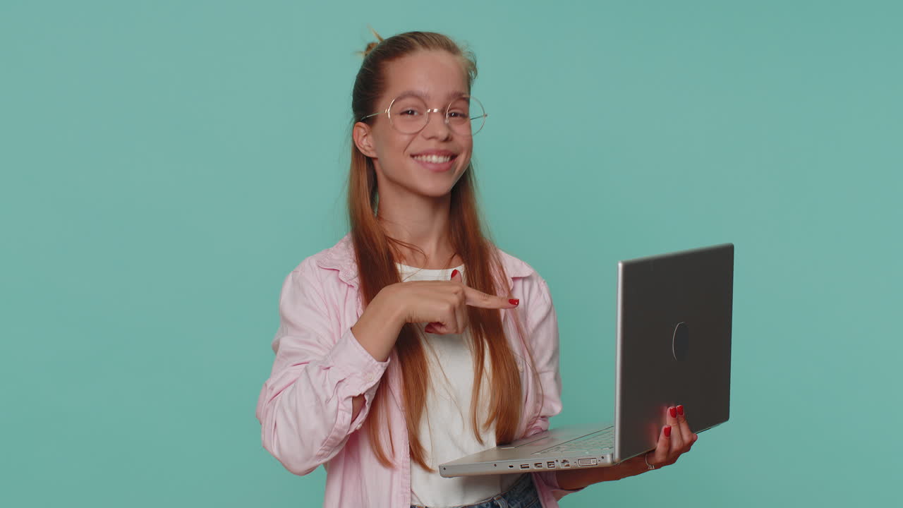 niña trabajando en línea en una computadora portátil, mostrando el pulgar a la cámara, retroalimentación positiva, como, ganar la lotería