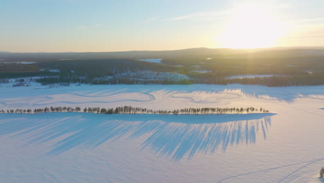 Lange-Schatten-über-Dem-Schneebedeckten-Lappland-Goldener-Sonnenaufgang-Treibende-Rennstreckenluftaufnahme