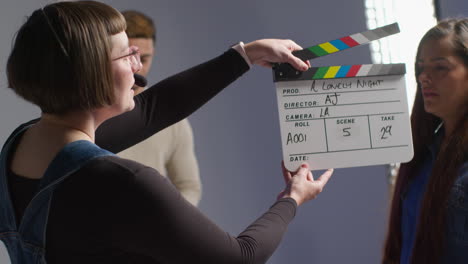 female production assistant on film set in studio using clapperboard or slate on movie or video as actors start scene 6