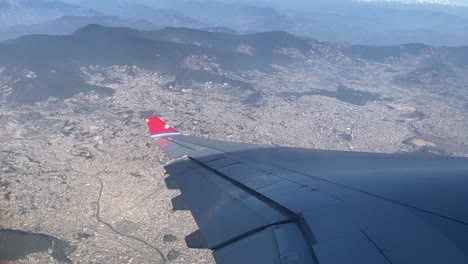 a beautiful high angle view of the city of kathmandu, nepal while looking out over the wing of a nepal airlines jet