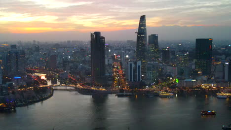 Ciudad-Ho-Chi-Minh-Vietnam-Al-Atardecer,-Vista-Aérea-Del-Paisaje-Urbano-Por-El-Río-Saigón-Al-Atardecer,-Edificios-Rascacielos-Calles,-Puentes-Y-Cielo-Dorado-En-Segundo-Plano