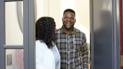 casal afro-americano feliz recebendo convidados em casa ensolarada