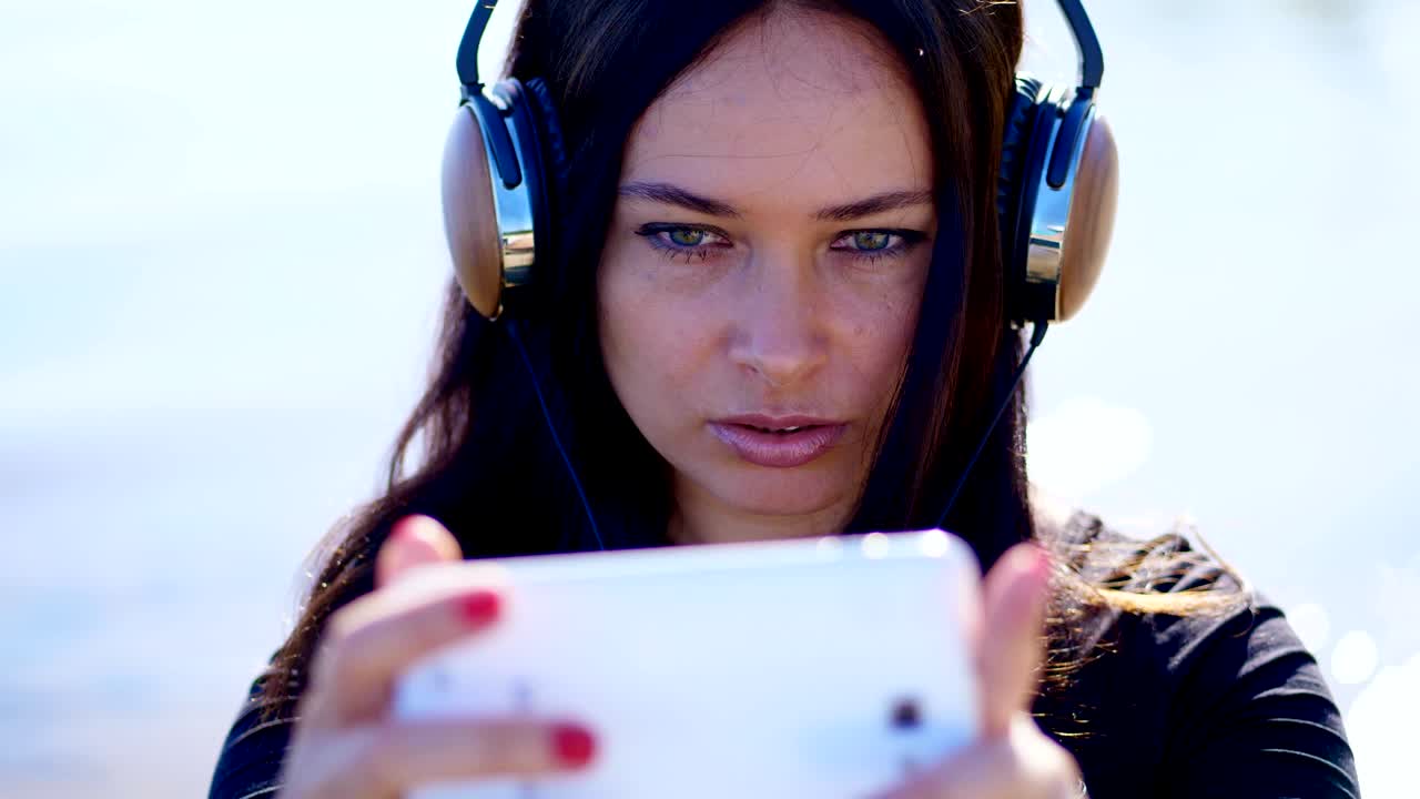 verano, al aire libre, retrato de una mujer hermosa, con cabello largo y oscuro, escuchando música en auriculares de un teléfono móvil, dispositivo, se retira en el teléfono, hace selfies