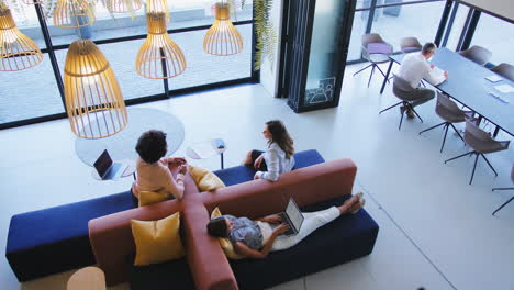 overhead view of modern open plan office with staff working around table and breakout seating area