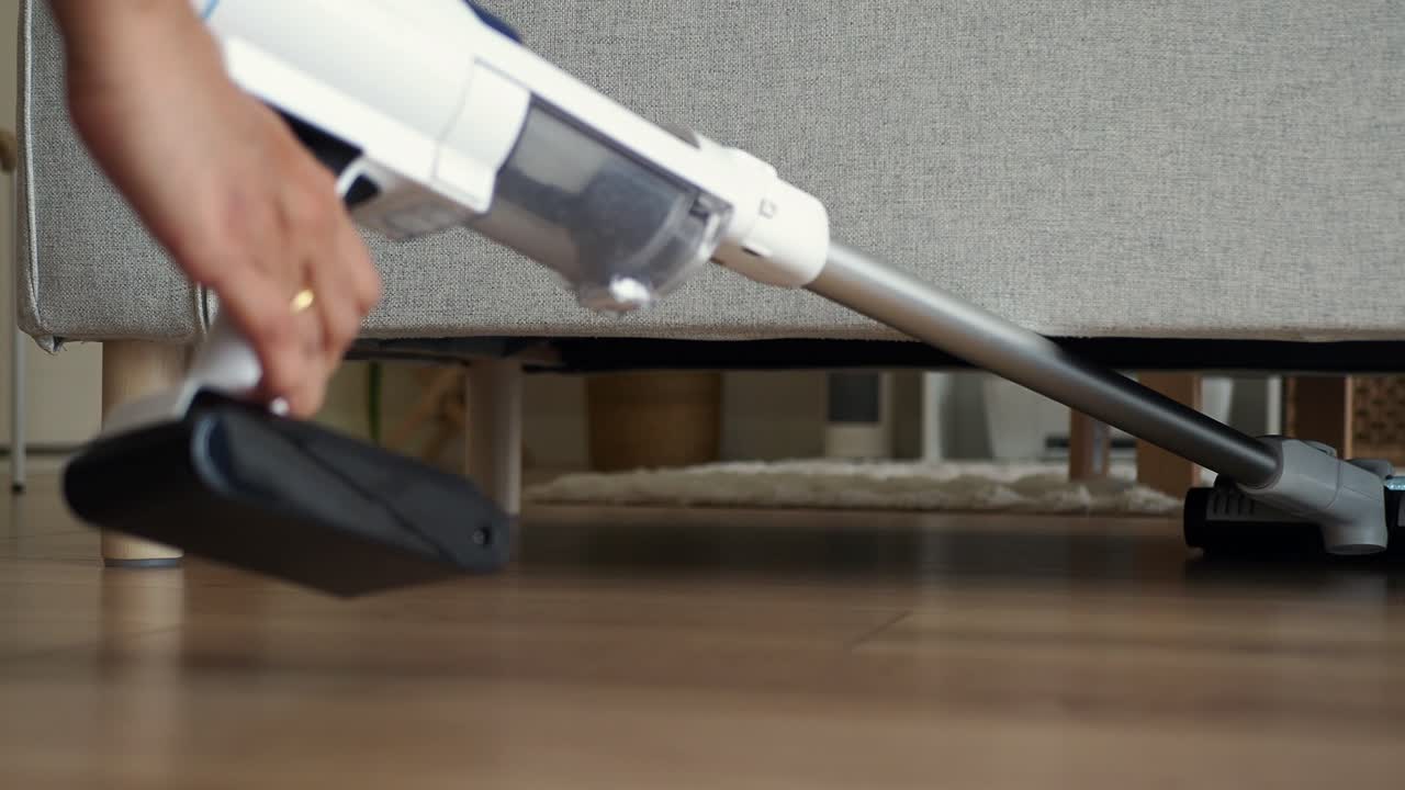 Bezdrátový vysavač uklízející pod pohovkou na dřevěné podlaze