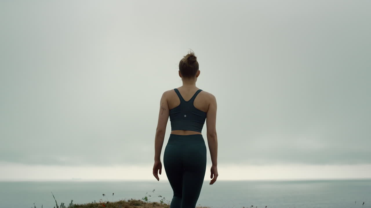 Ung sportsudøver bestiger en bakketop, set bagfra. Sporty pige går op ad en strandbakke.