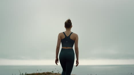 young sportswoman climb hilltop back view. sporty girl walking up beach hill.