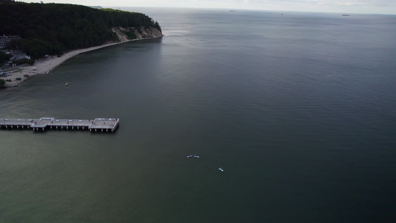 воздушная орбита у пирса орлово в гдыне с людьми, катающимися на паддлбордах на закате