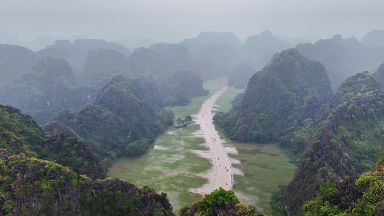 Misty aerial view over Hang Mua and Tam Coc in Ninh Binh, Vietnam, revealing limestone karst mountains and a winding river cutting through the scenic valley landscape