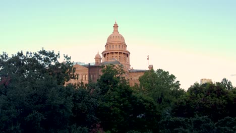 en el centro de austin, el edificio de la capital del estado de texas, un avión no tripulado volando volando a través de los árboles del patio en el ala oeste del edificio