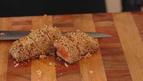 Handheld-motion-close-up-shot-capturing-sliced-salmon-tataki-on-the-chopping-board,-fish-fillet-covered-in-delicious-seared-brown-curst-of-white-sesame-seeds-on-the-outer-layer-and-raw-in-center