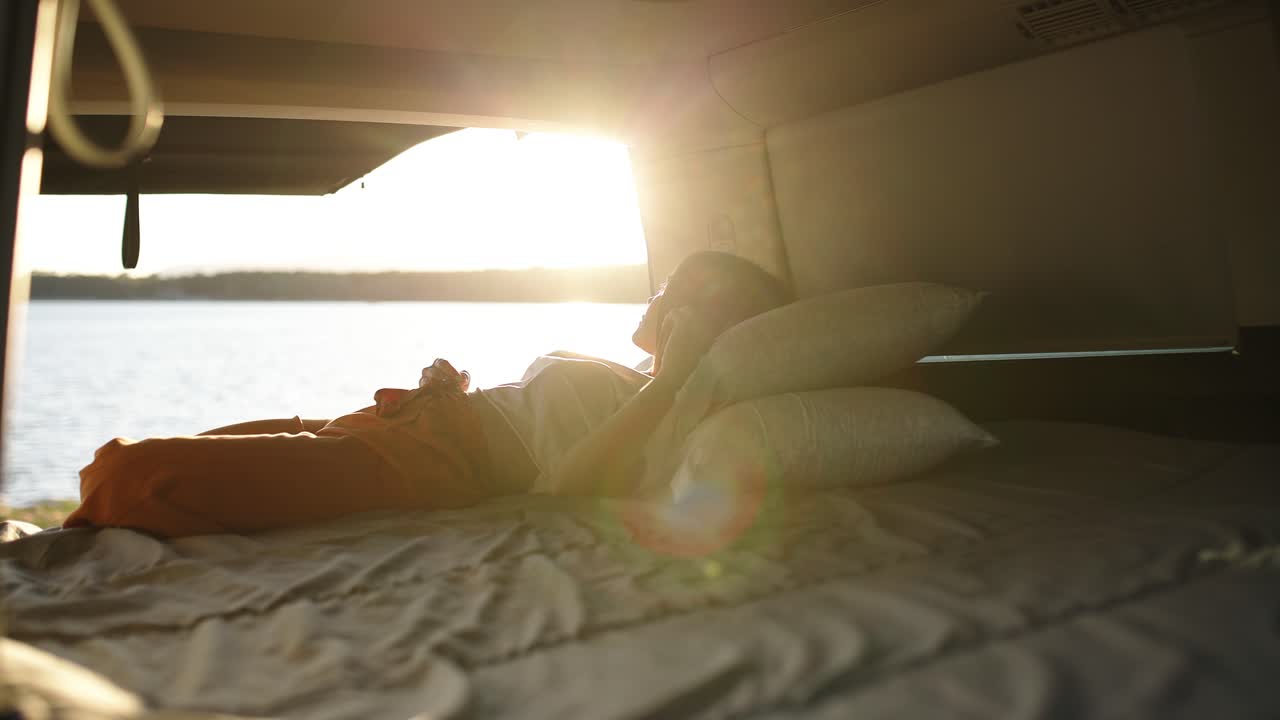 Kvinde slapper af i autocamperens seng ved solnedgang ved søen.