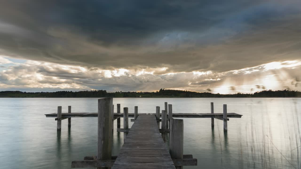 Stormy clouds move over a lake. Sunbeams break through the clouds and shine on the landscape. The storm passes. Beautiful nature, captured from a jetty. Time-lapse.