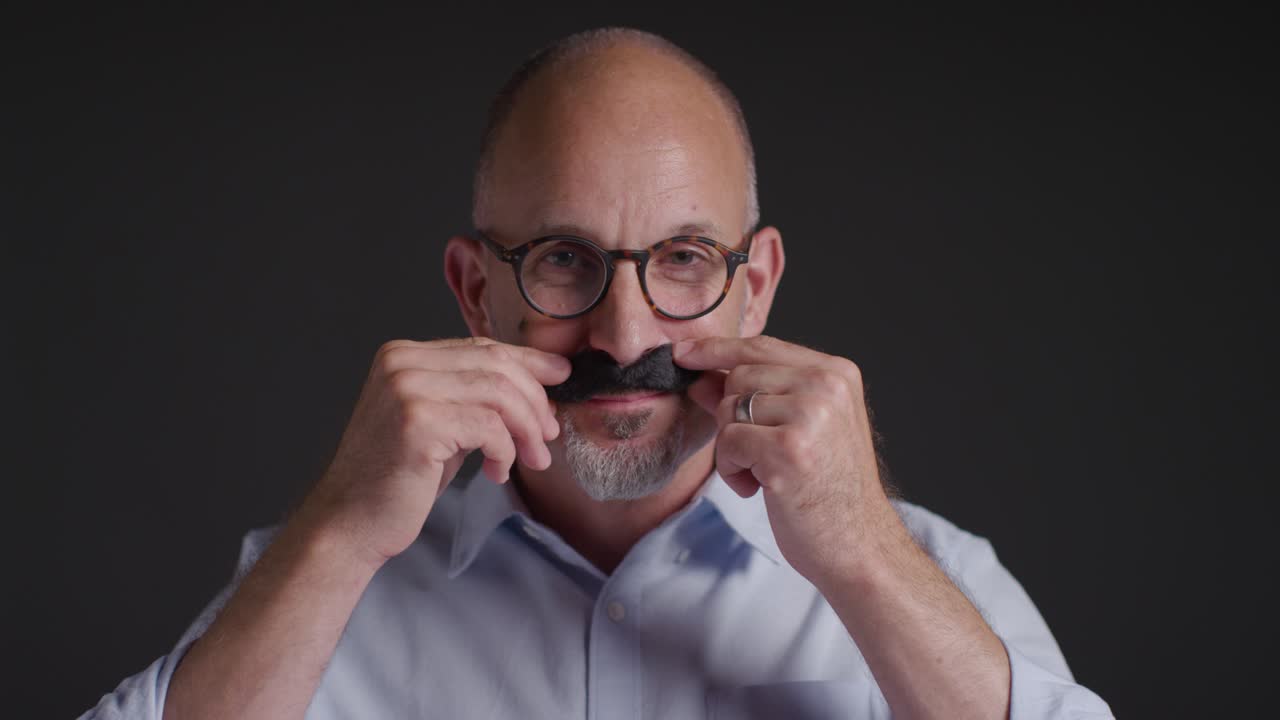 Portrait Of Mature Man Wearing Fake Moustache Symbolizing Support For Movember Promoting Men's Health And Cancer Awareness