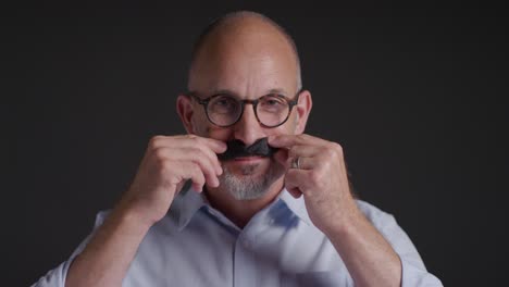 portrait of mature man wearing fake moustache symbolizing support for movember promoting men's health and cancer awareness