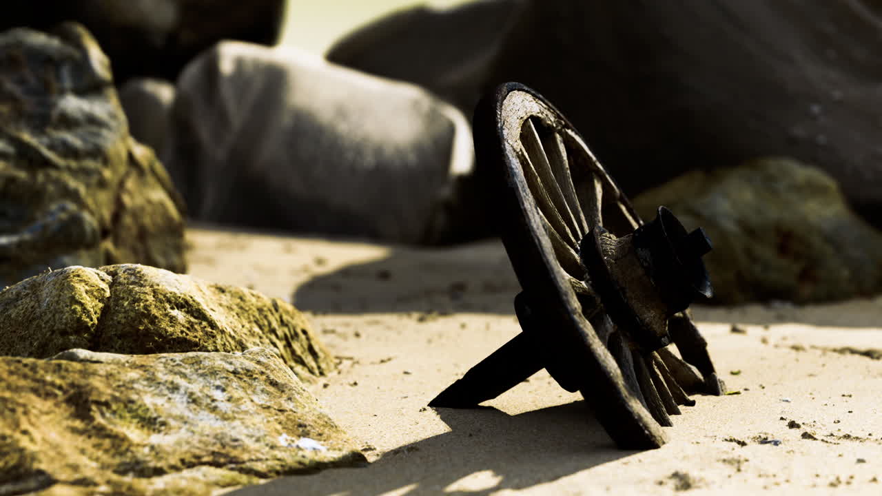 Old wheel fragment rests among rocks on a sunlit sandy shore