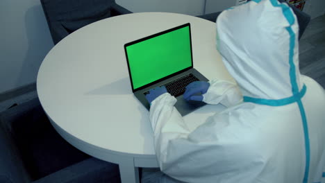 concepto de portátil de pantalla verde - trabajador médico con traje protector mira en la pantalla del ordenador