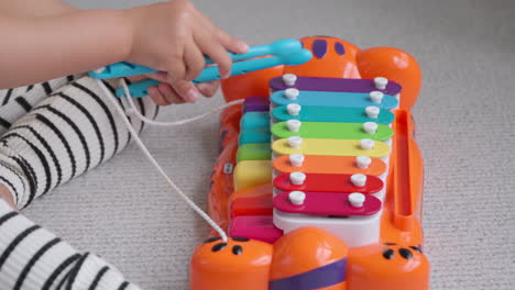 Manos-Cercanas-De-Una-Niña-Pequeña-Y-Activa-Tocando-Un-Piano-De-Juguete-Y-Un-Instrumento-Musical-De-Xilófono-Para-Niños-Sentados-En-El-Suelo-En-Casa---Cámara-Lenta