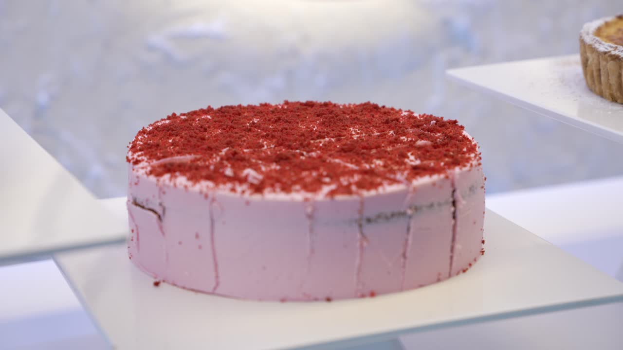 Sliced red velvet cake with pink frosting and crumbs on white display stand