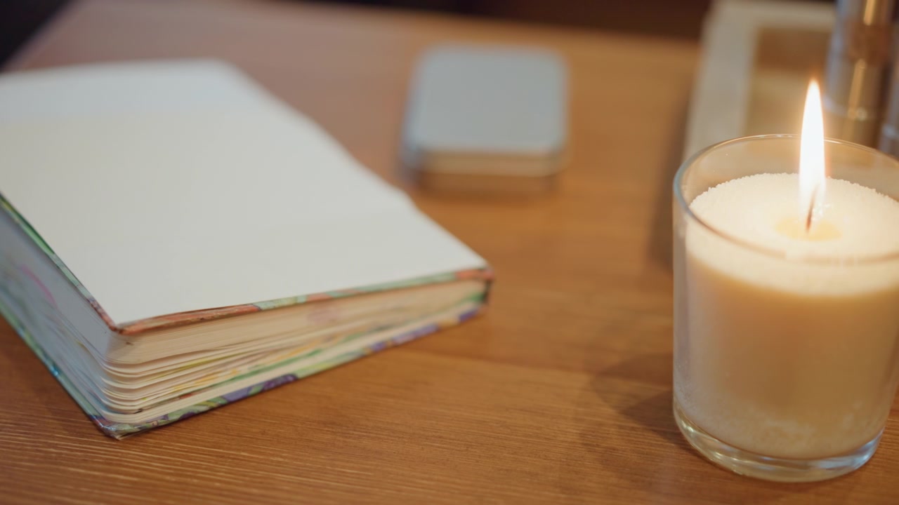Close up of blank notebook with colorful edges on wooden surface as candle flame flickers nearby soft lighting table pages flickering light closeup stationary