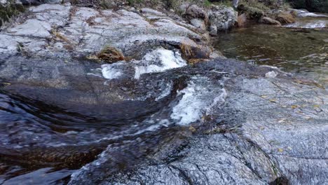 Corriente-De-Agua-Que-Fluye-Sobre-La-Superficie-De-Algunas-Rocas-Creando-Una-Especie-De-Rápidos-Y-Cascadas