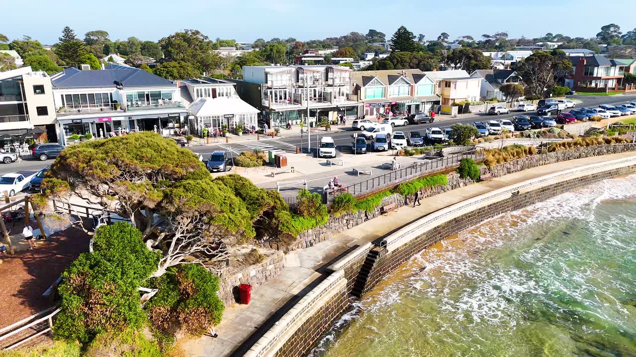 Aerial footage captures Point Lonsdale's coastline, showcasing vibrant greenery, seaside architecture, and gentle waves under bright daylight