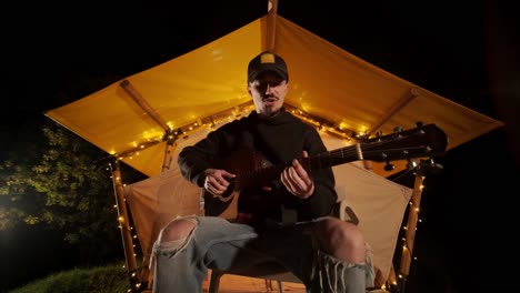 man plays the guitar and sings songs in a tent with light bulbs