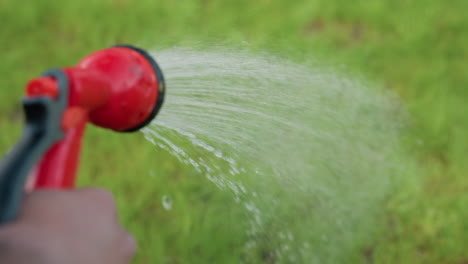 close up hand watering lush grass with garden hose, droplets sparkling on blades in crisp blur background under bright sunlight, capturing nurturing outdoor care scene of summer hydration ritual