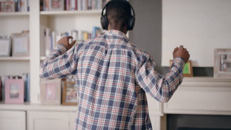 funny african american man dancing at home wearing headphones celebrating success listening to music having fun crazy dance in living room happy lifestyle 4k