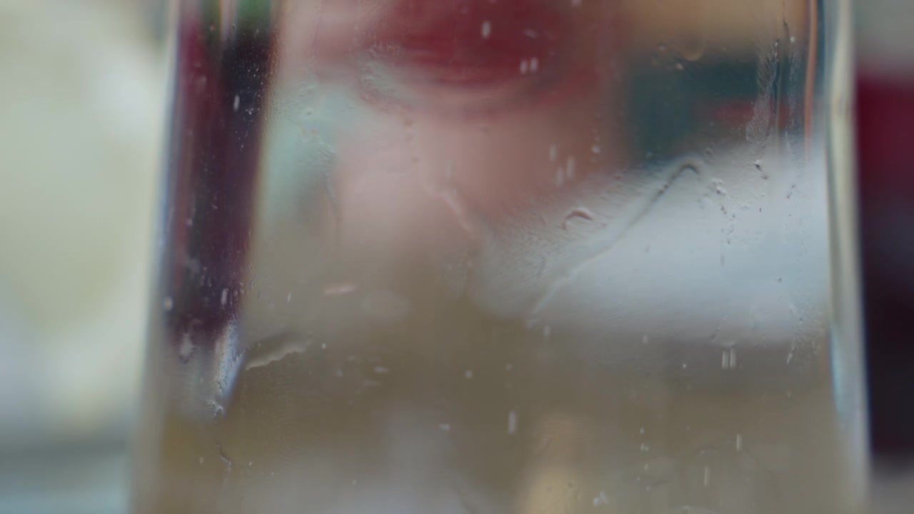 Extreme close up of condensation beads running down a chilled glass, warm blurred colors moving behind. Abstract refreshing texture for beverage and summer heat themes.